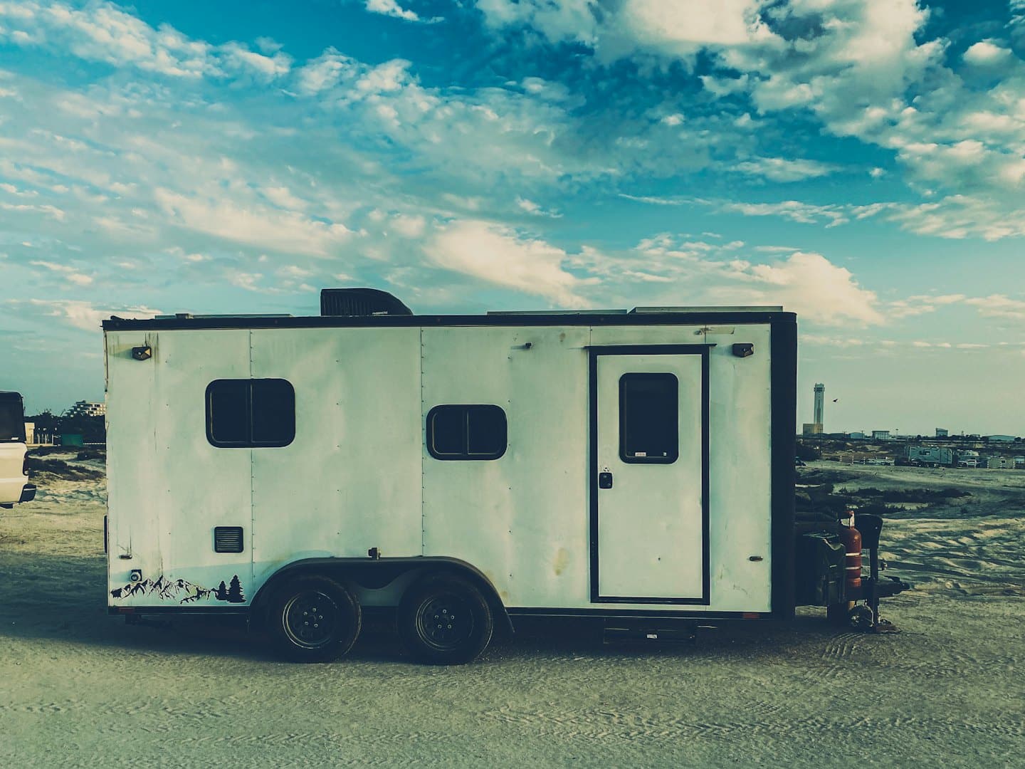 A white utility trailer parked on gravel near a distant city.