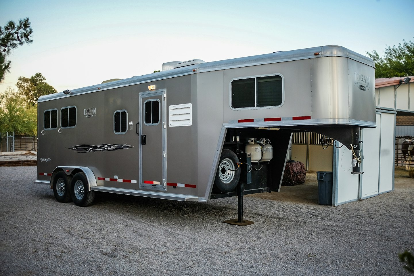 Modern grey horse trailer parked on gravel lot.